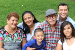 A multigenerational Hispanic family sitting outside on the grass who may be facing elder care challenges