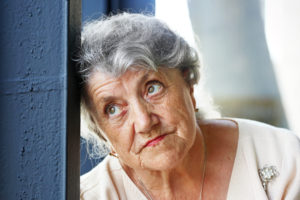 An elderly Hispanic woman looking upset out of a window