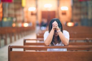 A Hispanic woman praying in a church, highlighting the idea of bible verses for caregivers